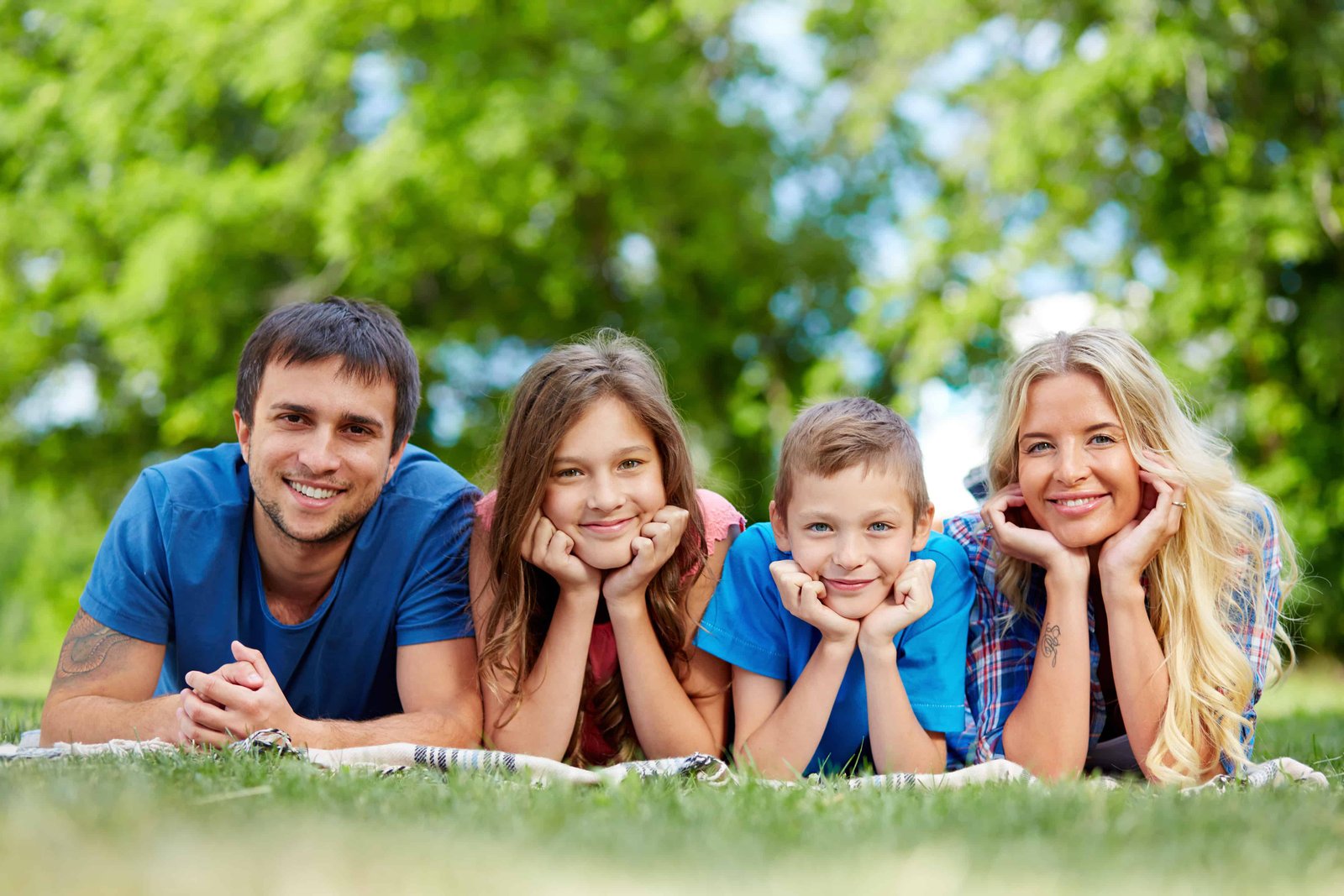 Photo of happy family of four lying on grass during summer rest